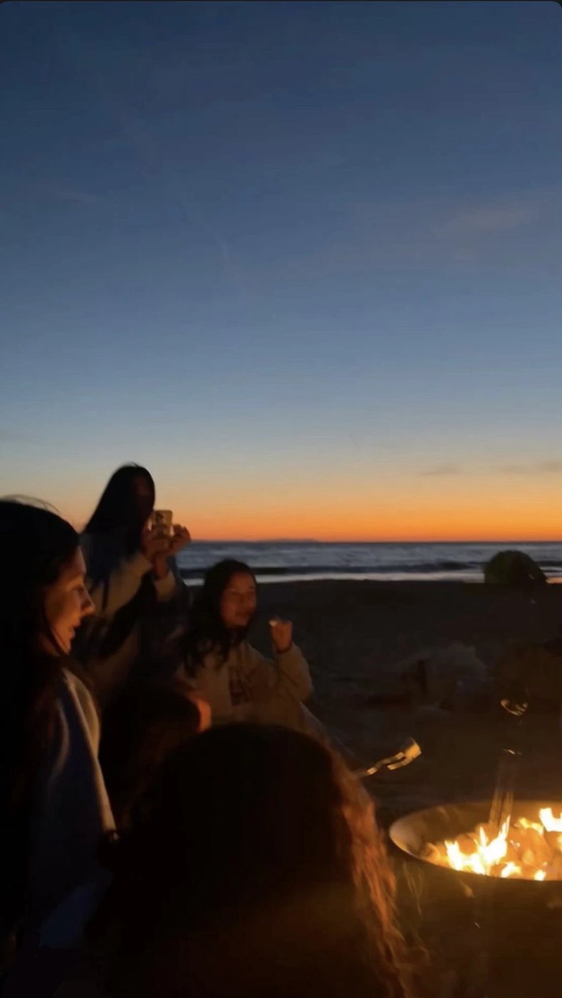 Friends gathered around a fire pit on the beach at sunset